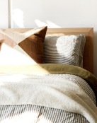 swath of sunlight shines across a well made bed and bedside table with a vase of cotton plants